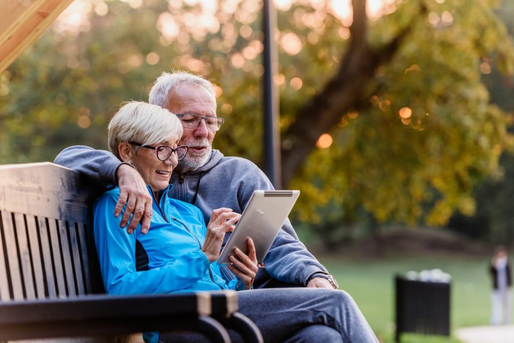 older couple sitting on a park bench looking scrolling and looking at tablet -phone -computer